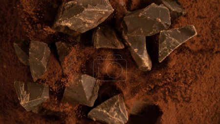 Foto de Congelar el movimiento del grupo volador de piezas de chocolate crudo. Caer en polvo de cacao. - Imagen libre de derechos