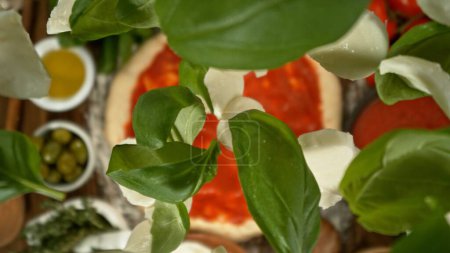 Foto de Deliciosa pizza con ingredientes voladores de arriba. Congelar el movimiento de las hojas de albahaca voladora en pizza. Concepto de preparación de alimentos, masa cruda. - Imagen libre de derechos