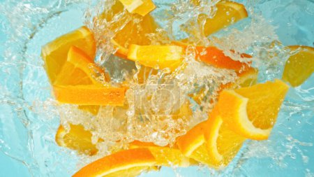 Téléchargez les photos : Congeler le mouvement des tranches d'orange tombant dans l'eau, éclaboussures. Tir aérien de fruits frais, isolé sur fond bleu. - en image libre de droit
