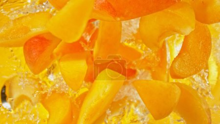 Foto de Freeze Motion of Flying Apricots into Water, Colored Background. Concept of Flying Fresh Fruit, Splashing into Water. - Imagen libre de derechos