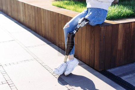 Photo for Female with prosthetic leg sitting in city. Woman with prosthetic leg drinking coffee. Woman with leg prosthesis equipment. - Royalty Free Image