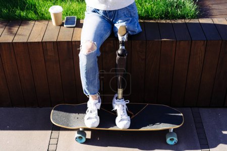 Photo for Close up of women prosthetic leg on skateboard in city. Disabled woman with prosthetic leg sitting on wood bench. Woman with leg prosthesis equipment. - Royalty Free Image