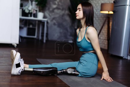 Photo for Lady with prosthesis leg demonstrates resilience during yoga session. Young woman enhances physical and mental health through sports at home - Royalty Free Image