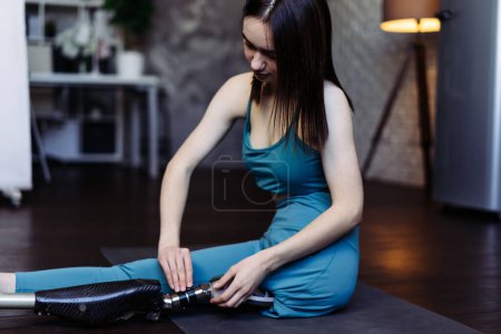 Photo for Young woman with disability starts sports routine putting on prosthetic limb. Lady in sportswear prepares for regular physical activity to tone muscles - Royalty Free Image