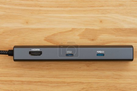 Foto de Hub USB-C portátil para conectar dispositivos USB con un cable que se carga en el escritorio de madera - Imagen libre de derechos