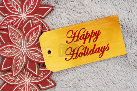 Photo for Happy Holidays greeting on a gift tag with wood poinsettias on gray plush material - Royalty Free Image