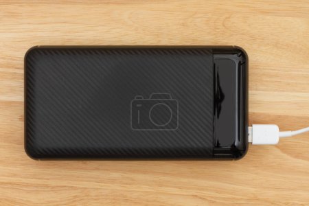 Photo for Portable power bank for charging USB devices with a cable charging on wood desk - Royalty Free Image