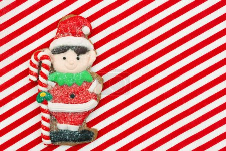 Téléchargez les photos : Joli elfe en pain d'épice sur fond de vacances à rayures rouges et blanches pour votre message d'hiver ou saisonnier - en image libre de droit