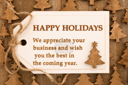 Foto de Mensaje de Felices Fiestas en una etiqueta de regalo de madera sobre árboles en madera envejecida - Imagen libre de derechos