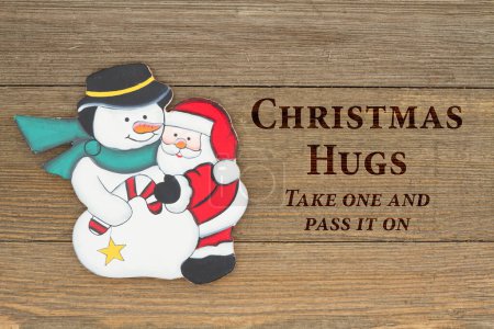 Photo for Old fashion Christmas message, A retro snowman and Santa Claus hugging on weathered wood background with text Christmas Hugs take one and pass it on - Royalty Free Image