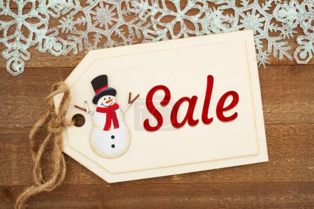 Foto de Sale message on a wood gift tag and snowman with snowflakes on weathered wood - Imagen libre de derechos