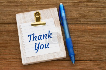 Photo for Thank you message on lined paper on a chipboard with a pen on weather wood desk - Royalty Free Image
