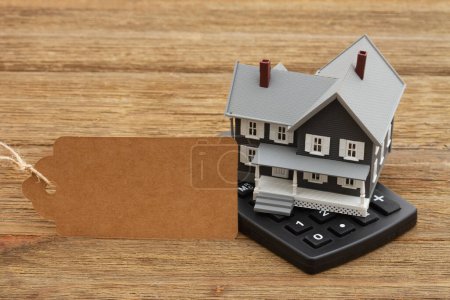 Téléchargez les photos : Mortgage calculator and gift tag with a house on a calculator on a wood desk - en image libre de droit