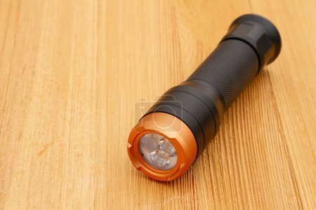 Téléchargez les photos : Black and bronze LED flashlight on wood table for your emergency ready kit - en image libre de droit