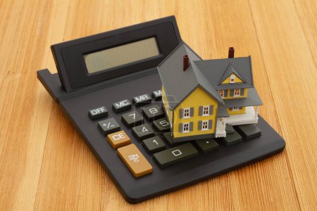Photo for Mortgage calculator with a house on a calculator on a wood desk - Royalty Free Image