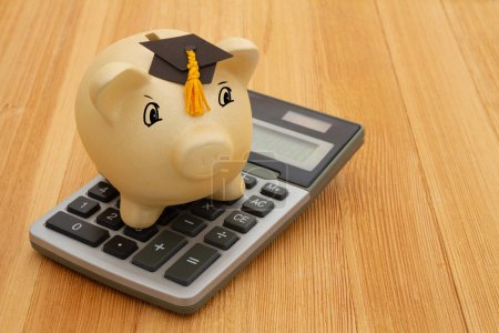 Photo for Gold piggy bank with a grad cap and calculator on wood desk for your money or saving for school - Royalty Free Image
