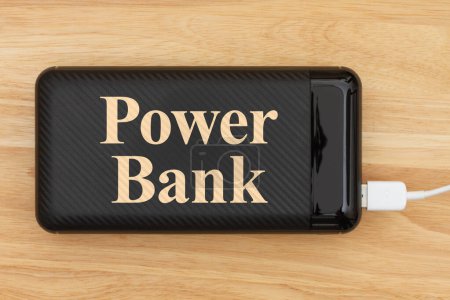 Photo for Portable power bank for charging USB devices with a cable charging on wood desk - Royalty Free Image