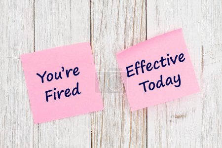 Photo for Youre Fired Effective Today message on yellow sticky note on weathered wood for your job firing - Royalty Free Image