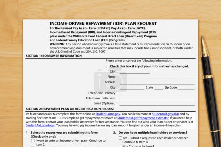 Téléchargez les photos : Formulaire de demande d'allègement du paiement du prêt étudiant fédéral américain sur un bureau en bois - en image libre de droit