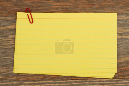 Foto de Pila de tarjetas de índice de papel amarillo retro con clip de papel en escritorio de madera con espacio de copia para su mensaje - Imagen libre de derechos