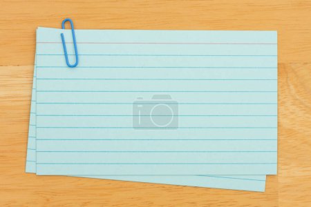 Foto de Pila de tarjetas de índice de papel azul retro con clip de papel en escritorio de madera con espacio de copia para su mensaje - Imagen libre de derechos