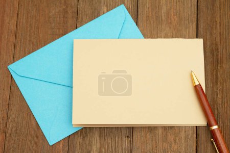 Foto de Tarjeta de felicitación en blanco con sobre azul y bolígrafo en madera envejecida - Imagen libre de derechos