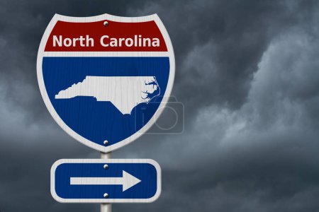 Foto de Viaje por carretera a Carolina del Norte, rojo, blanco y azul señal de carretera interestatal con la palabra Carolina del Norte y el mapa de Carolina del Norte con el fondo del cielo tormentoso - Imagen libre de derechos