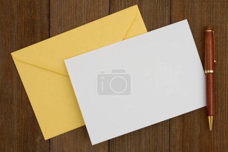 Foto de Tarjeta de felicitación en blanco con sobre amarillo y bolígrafo en madera envejecida - Imagen libre de derechos