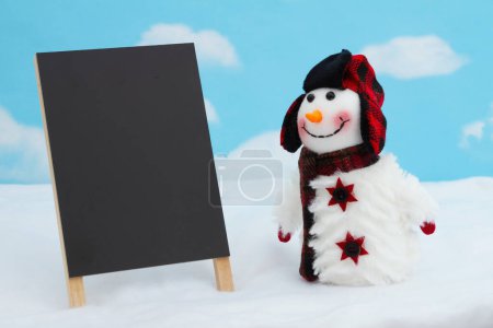 Téléchargez les photos : Bonhomme de neige avec chapeau et écharpe et tableau blanc avec neige pour les vacances ou le message de Noël - en image libre de droit