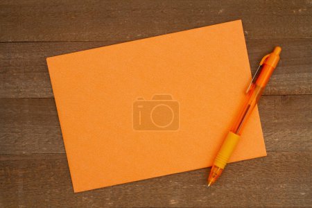 Foto de Tarjeta de felicitación en blanco y bolígrafo naranja sobre madera envejecida - Imagen libre de derechos