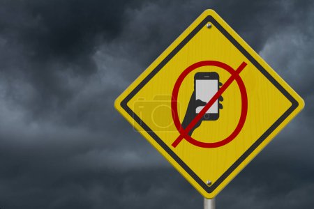 Foto de No hay mensajes de texto o teléfono celular mientras conduce en señal de advertencia con cielo tormentoso - Imagen libre de derechos
