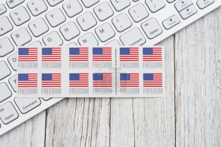 Photo for SC, USA Mar 2024. Illustrative editorial image of computer keyboard with book of US forever stamps on weathered wood desk - Royalty Free Image