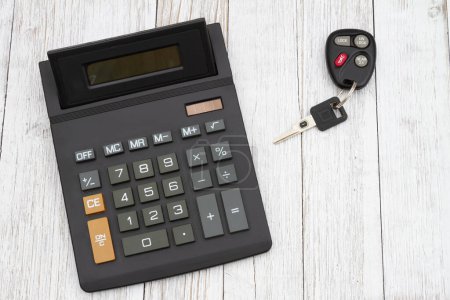 Téléchargez les photos : Une calculatrice noire avec clés de voiture grand écran sur un bureau en bois altéré - en image libre de droit