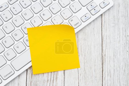 Foto de Teclado de ordenador con una nota amarilla pegajosa en el escritorio de madera envejecida - Imagen libre de derechos