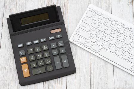 Foto de Una calculadora negra con teclado de ordenador blanco sobre escritorio de madera envejecida - Imagen libre de derechos