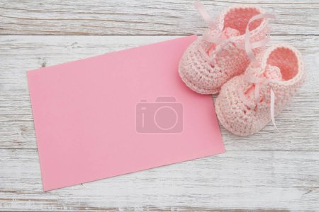 Téléchargez les photos : Chaussons bébé rose avec carte de vœux rose sur un bois altéré avec de l'espace pour vous message - en image libre de droit