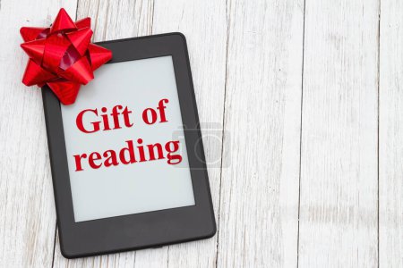 Foto de El regalo de leer con un lector con lazo de regalo rojo en una vieja mesa erosionada - Imagen libre de derechos