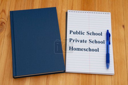 Foto de Escuelas públicas vs privadas vs en casa con libro azul antiguo retro con bloc de notas y bolígrafo en un escritorio - Imagen libre de derechos