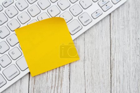 Foto de Teclado de ordenador con una nota amarilla pegajosa en el escritorio de madera envejecida - Imagen libre de derechos