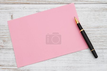 Foto de Tarjeta de felicitación rosa en blanco con bolígrafo sobre madera envejecida - Imagen libre de derechos