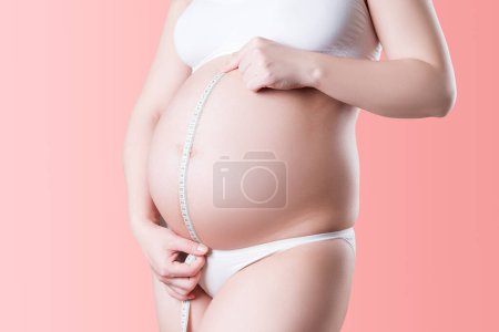 Photo for Pregnant woman with measuring tape in white underwear on pink background, pregnancy concept - Royalty Free Image