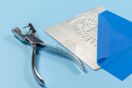 Photo for Dental hole punch, the rubber dam and the metal plate on the blue background. Medical tools concept. - Royalty Free Image