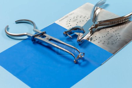 Photo for Dental hole punch, the metal plate, the rubber dam and the rubber dam forceps on the blue background. Medical tools concept. Top view. - Royalty Free Image
