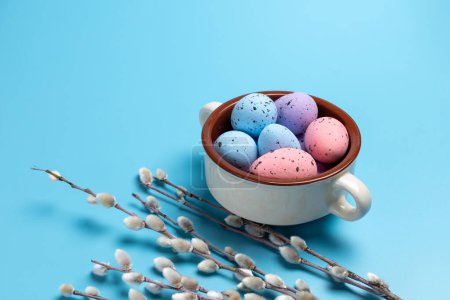 Foto de Cuenco con huevos de Pascua de colores y ramas de sauce con amentos en el fondo azul. Vista superior. - Imagen libre de derechos
