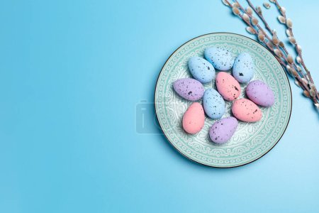 Plato con huevos de Pascua de colores y ramas de sauce con amentos en el fondo azul. Vista superior.