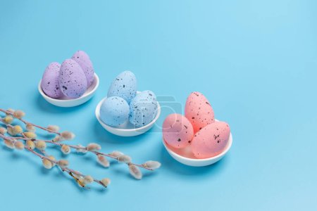 Foto de Platillos de porcelana con huevos de Pascua de colores y ramas de sauce con amentos en el fondo azul. Vista superior. - Imagen libre de derechos