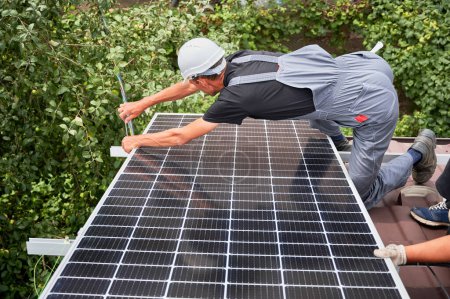 Téléchargez les photos : Les hommes montent des modules solaires photovoltaïques sur le toit de la maison. Electriciens en casques installant le système de panneaux solaires à l'extérieur. Concept d'énergies alternatives et renouvelables. - en image libre de droit