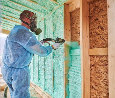 Männliche Bauarbeiter isolieren Holzrahmenhaus. Mann Arbeiter sprüht Polyurethan-Schaum innerhalb der zukünftigen Hütte, mit Mehrkomponenten-Pistole. Bau- und Dämmkonzept.