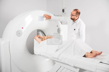 Foto de Tomografía computarizada médica o escáner de resonancia magnética. Radiólogo masculino presiona botón de resonancia magnética para examinar paciente femenino. - Imagen libre de derechos