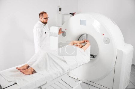 Téléchargez les photos : Medical computed tomography or MRI scanner. Male radiologist presses MRI button to examine female patient. Concept of healthcare and modern diagnostics. - en image libre de droit
